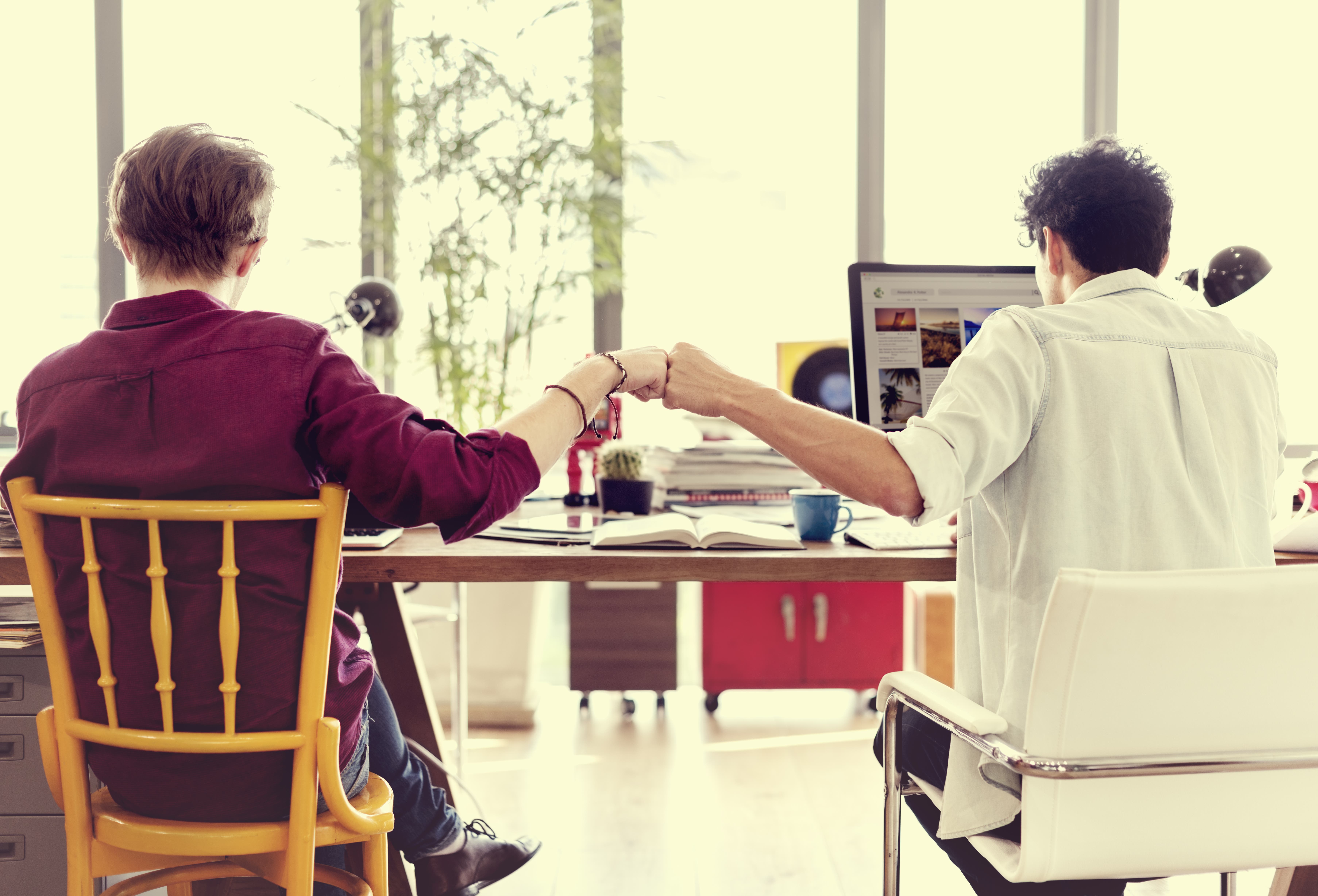 Coworkers bump fists at work desk