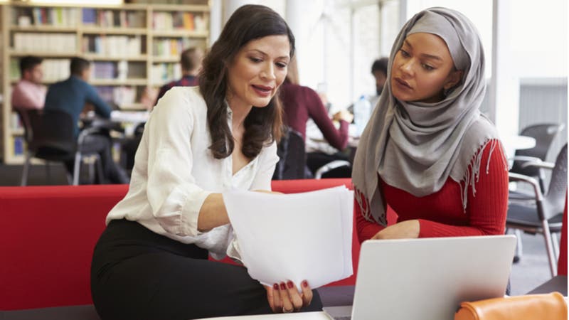 Woman explains paperwork to younger woman in library