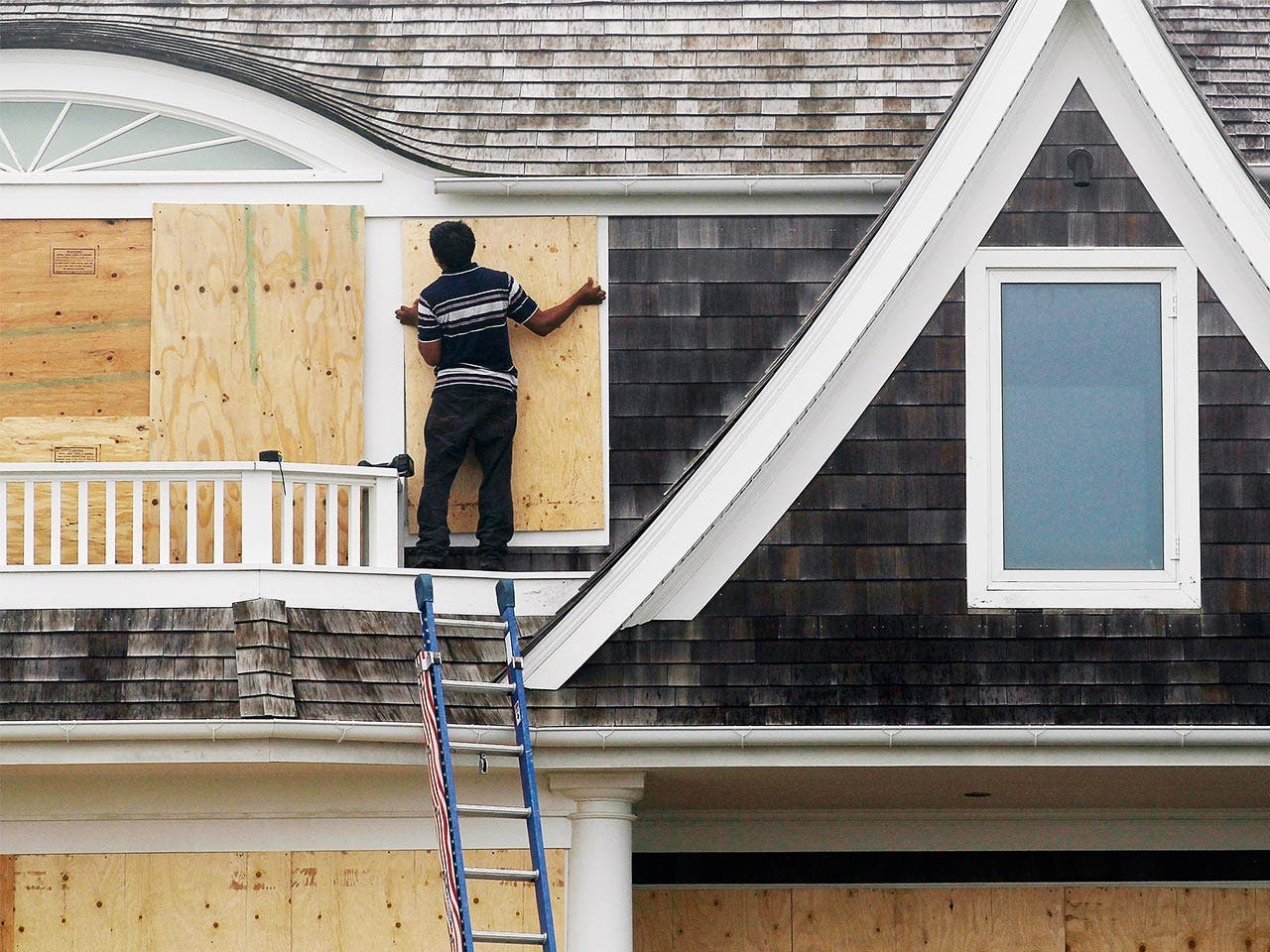Man installing plywood over windows to avoid damage