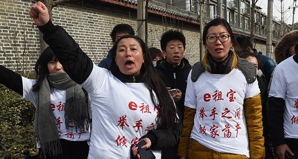 Investors in Chinese online peer-to-peer lender Ezubao chant slogans during a protest in Beijing on February 4, 2016. The protest came days after China announced that 21 people had been arrested on suspicion of defrauding around 900,000 people of more than 50 billion yuan (7.6 billion USD), after Ezubao turned out to be a giant Ponzi scheme. The T-shirts read 'Ezubao: Raise hands, lose a family fortune', a play on the company's slogan. AFP PHOTO / GREG BAKER / AFP / GREG BAKER