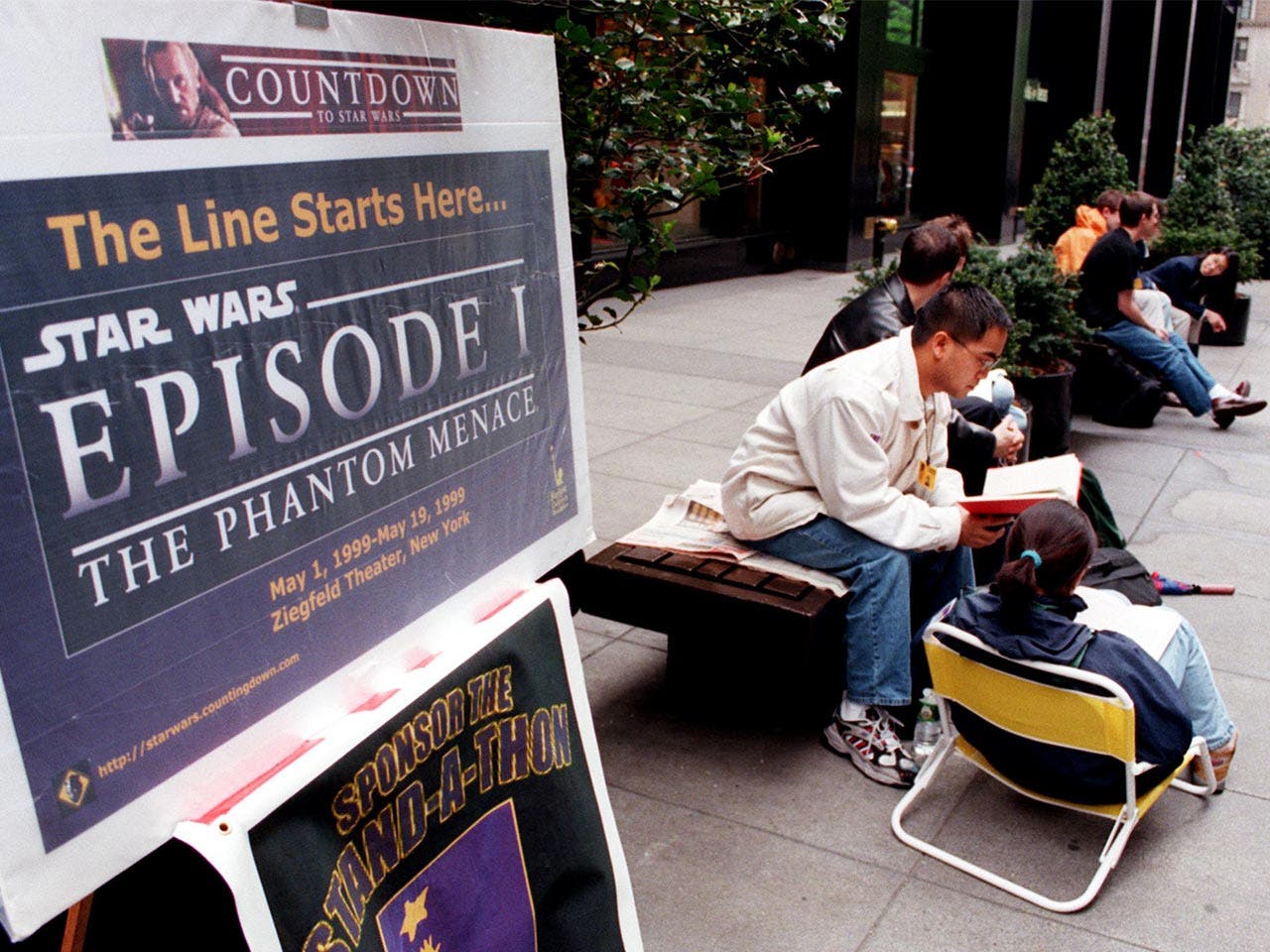 People sitting on a bench next to a “Star Wars: Episode I — The Phantom Menace” poster
