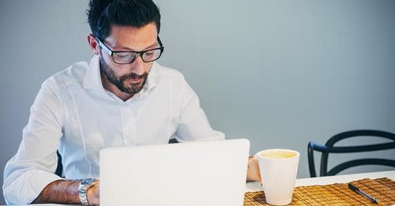 3 steps in deciding how much car you can afford Man in white shirt browsing laptop and drinking coffee | deimagine/Getty Images