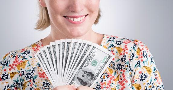 Smiling woman in floral shirt holding $100 bills