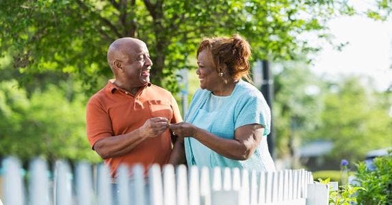 Spend savings early and get Social Security at 70? Happy couple standing outside by their picket fence | iStock.com/Susan Chiang