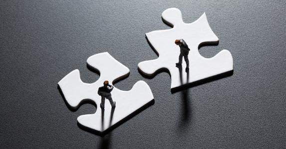 Businesesmen figurines standing on puzzle pieces © iStock
