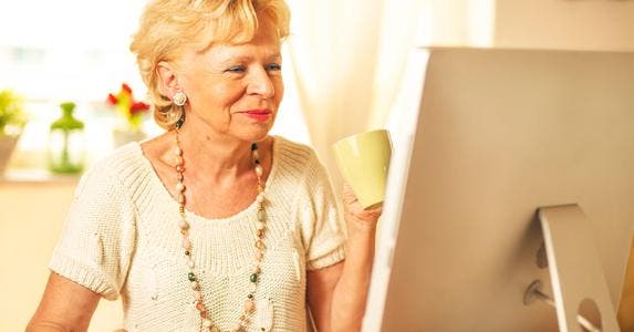 Senior woman holding cup of drink while on the computer © iStock