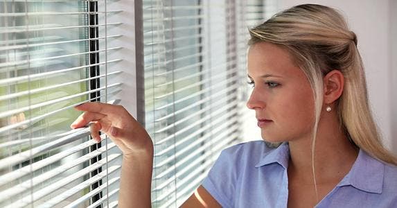 Woman peering through window blinds © auremar/Shutterstock.com