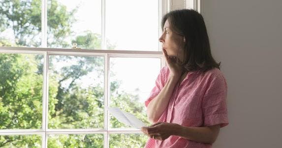 Debt collector seeks big fees on time share Woman looking out of the window holding a document | Cultura/Seb Oliver/Getty Images