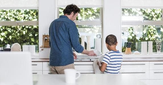 Plenty of reasons to sell your home for cash Dad and young son drying dishes in the kitchen | Portra Images/DigitalVision/Getty Images