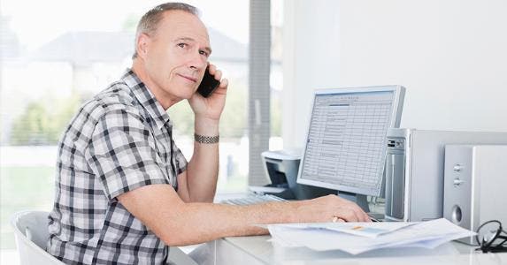 Man using phone while on computer © iStock