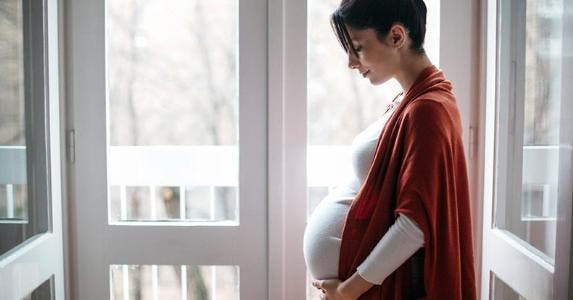 The health insurance gap that snares young moms Young pregnant woman standing by balcony door | iStock.com/momcilog