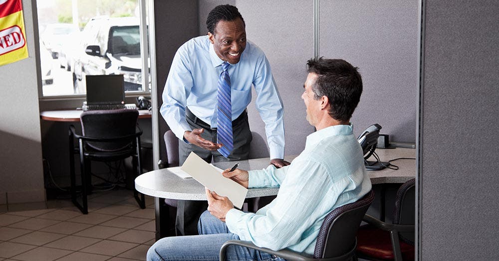 Car dealer talking to buyer at desk