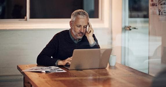 Owe taxes for using IRA funds to pay asset fees? Mature man in dining room reading laptop | iStock.com/PeopleImages