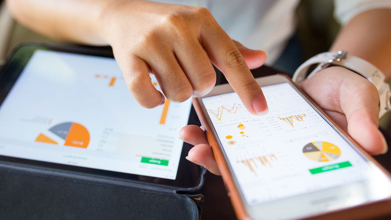 Person looking at investing apps on phone and tablet