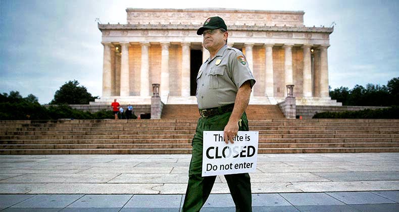 Government employee holding 'This site is CLOSED' sign | Andrew Harrer/Bloomberg/Getty Images