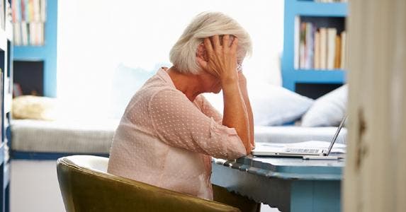 Woman holding her head, seated at table © iStock