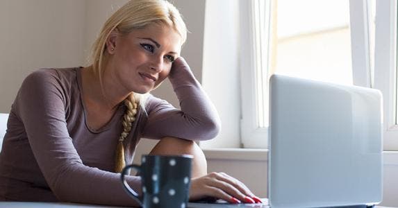 Young woman by window with her laptop © iStock