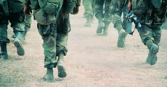Military members in uniform walking through desert terrain | Frank Rossoto Stocktrek/DigitalVision/Getty Images