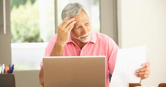 Don't get stiffed by freeloading kids Worried senior man in pink shirt reading paper, laptop on table | iStock.com/monkeybusinessimages