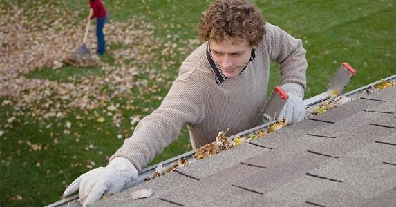 How to fortify your home against wildfires Man cleaning dead leaves from rain gutters | DreamPictures/VStock/Getty Images