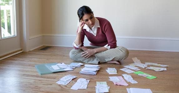 Answers to 10 tough debt questions Young woman sitting on floor staring at bills | iStock.com/LifesizeImages