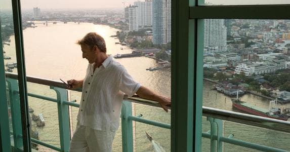 Can money buy happiness? It all depends Man using his phone on hotel balcony | iStock.com/AscentXmedia
