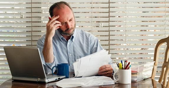 Worried mature man reading bills and papers in home office