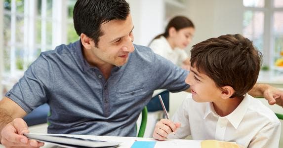 Dad helping young son with homework in kitchen table © iStock