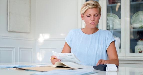 Woman at her kitchen table calculating bills © iStock