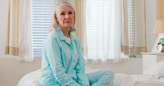 Pay $25K in credit card debt or file bankruptcy? Sad senior woman sitting on bed | Image Source/Getty Images