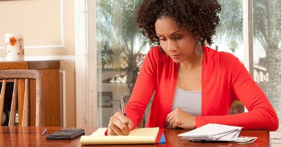 Woman on red cardigan writing down list or budget © iStock