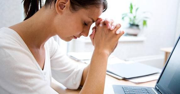 Woman resting her head on clasped hands © iStock