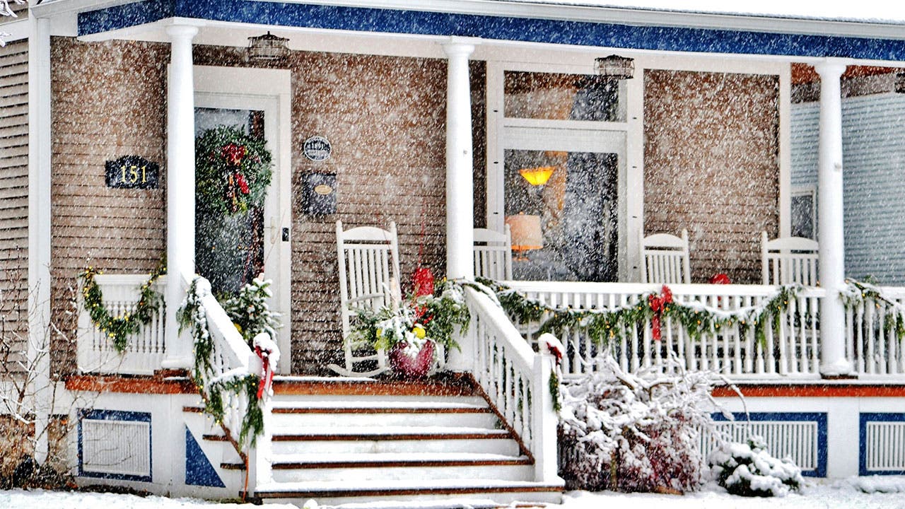 Snow falling on porch decorated for the holidays.