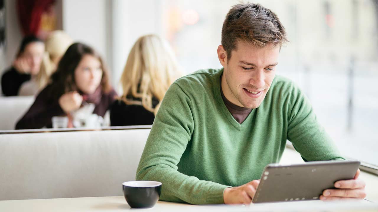 Young man wearing green jumper using tablet computer in cafe