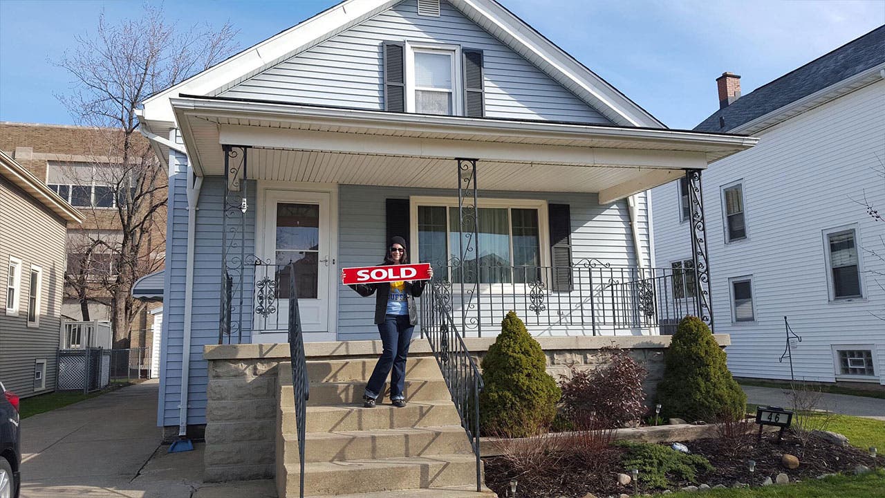 Woman holds up sold sign at new home