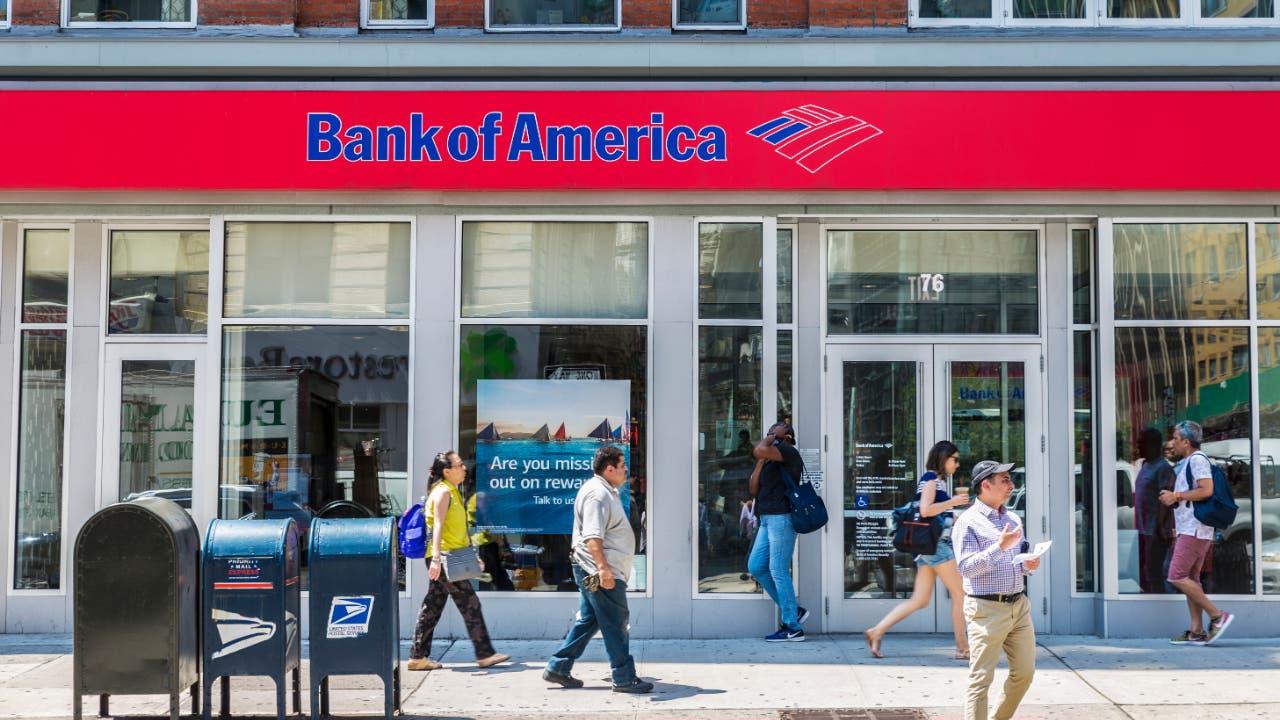People walking by a Bank of America storefront.