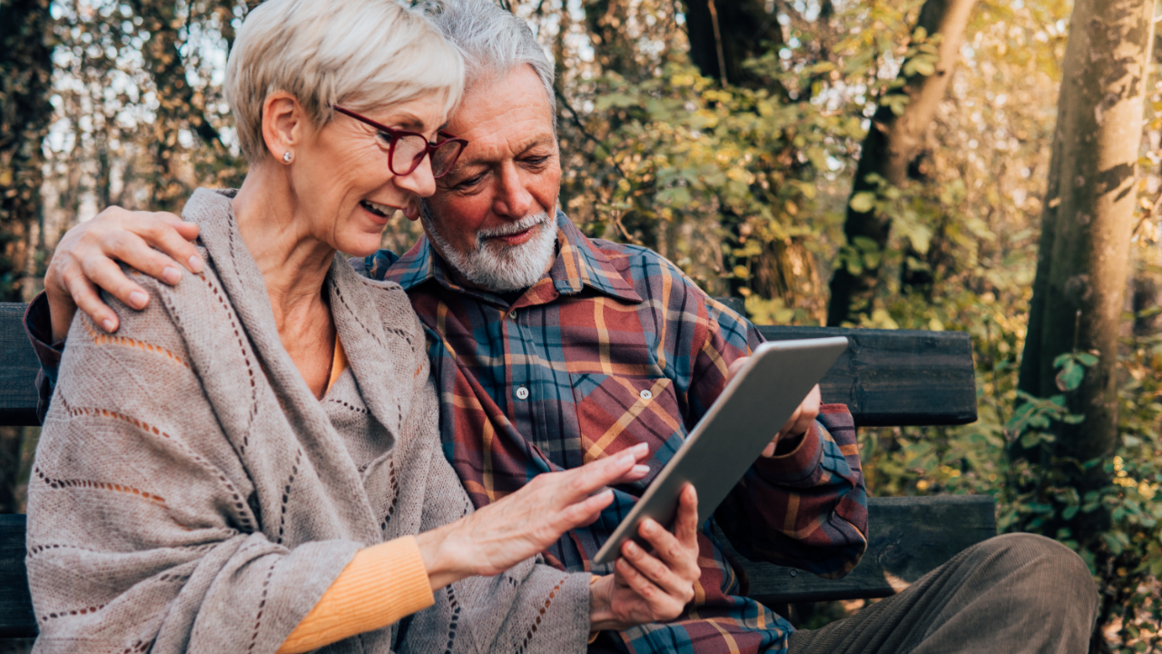 Senior couple looking at a tablet on a park bench