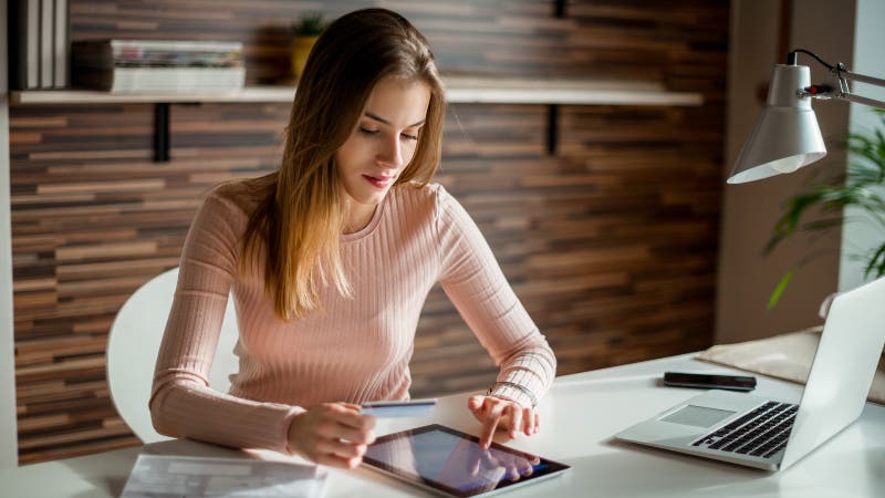 Woman at desk looking at tablet with credit card