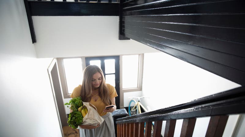 Woman walks up apartment stairs with groceries