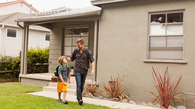 Father walking son to school in front of house