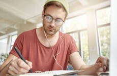 Young male college student doing paperwork while listening to music