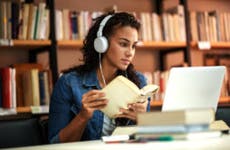Young college student studying in library while wearing headphones