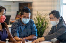 A mask-wearing couple reviews mortgage documents with a mask-wearing advisor.